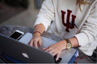 Indiana University uses Salesforce for recruiting, admissions, marketing, communications, graduate schools and HR case management. Image of student with computer. 