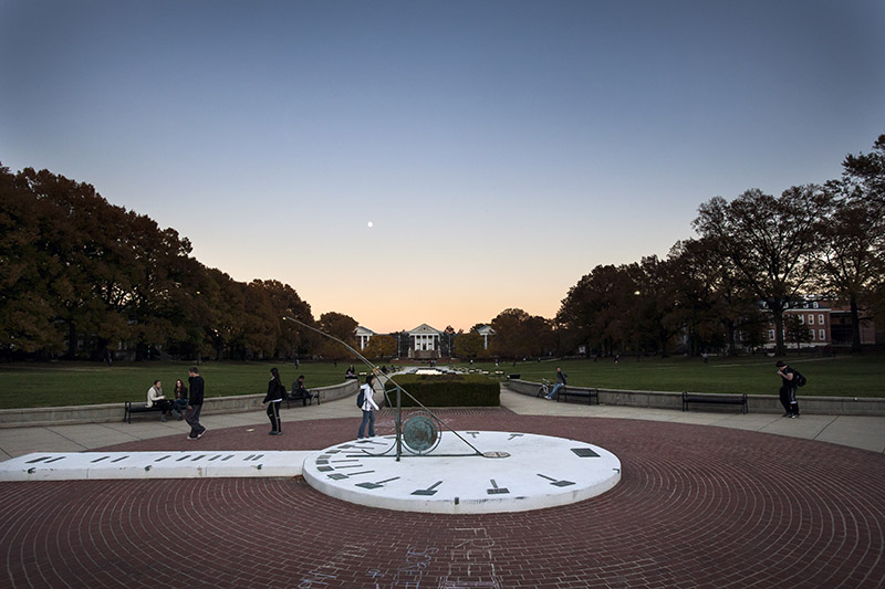 Sundial at dusk, with students walking by.