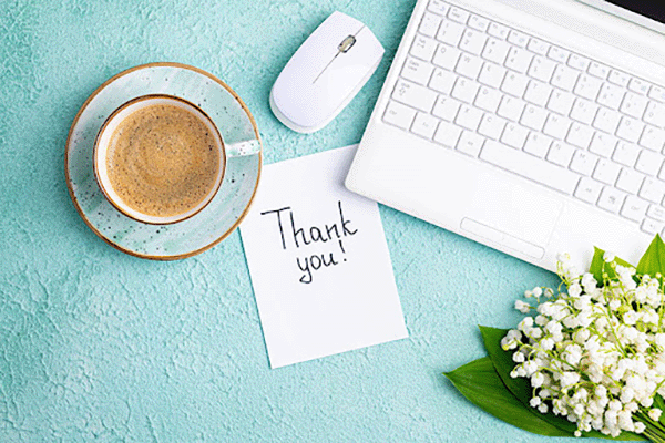 A top-down view of a laptop, cup of coffee, and a thank you note
