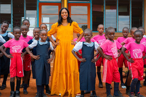 Woman standing and smiling with students in front of a classroom building
